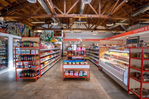 A bright, spacious grocery store interior with shelves stocked with snacks, beverages, and fresh produce.