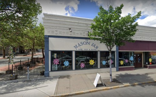 Exterior of The Mason Jar, a bake shop and bistro, featuring colorful flower decorations on windows and a sidewalk patio.