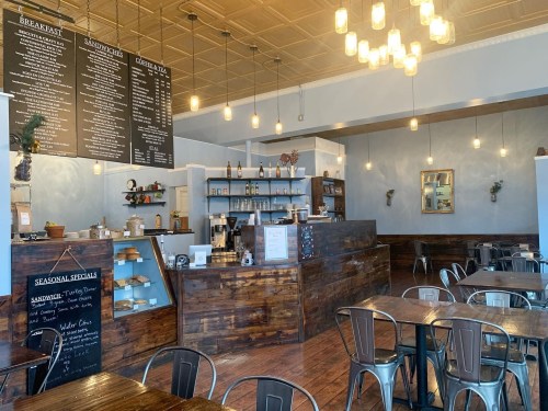 Cozy café interior with wooden furniture, a menu board, and warm lighting from hanging bulbs.