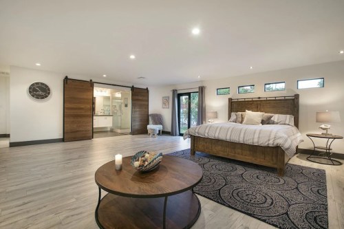 Spacious modern bedroom with a wooden bed, sliding doors, and a cozy seating area, featuring natural light and stylish decor.