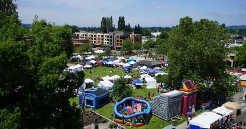 Aerial view of a lively outdoor festival with tents, inflatable attractions, and people enjoying a sunny day.