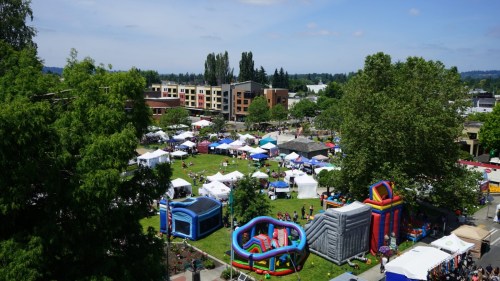 Aerial view of a lively outdoor festival with tents, inflatable attractions, and people enjoying the day in a park.