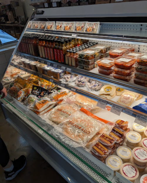 A refrigerated display case filled with various packaged foods, including sauces, snacks, and prepared meals.