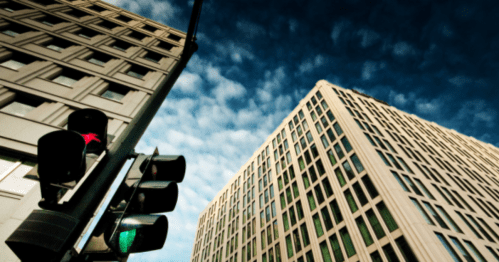 A traffic light in the foreground with two modern buildings and a cloudy sky in the background.