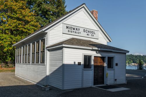 Historic Midway School building with large windows, set against a backdrop of trees and a lake.