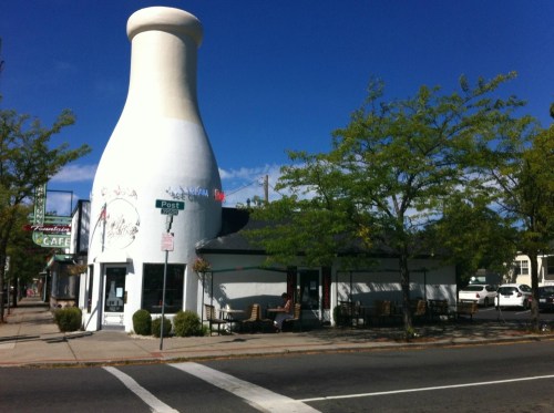 A quirky building shaped like a milk bottle, surrounded by trees and a clear blue sky.