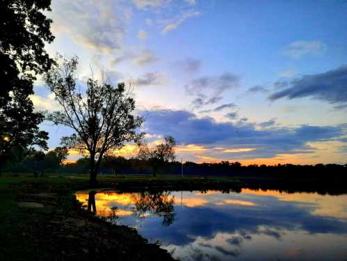 A serene lake at sunset, with colorful clouds reflecting on the water and trees lining the shore.