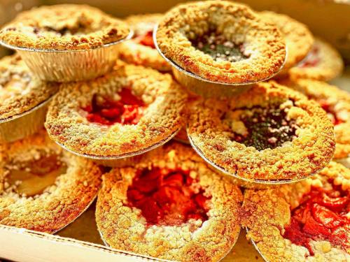 A close-up of assorted fruit pies with crumbly crusts, arranged in a box, showcasing various fillings.