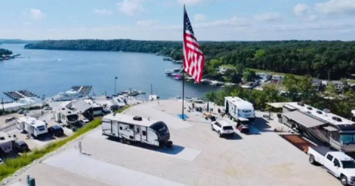 Aerial view of a lakeside RV park with a large American flag and boats in the water.