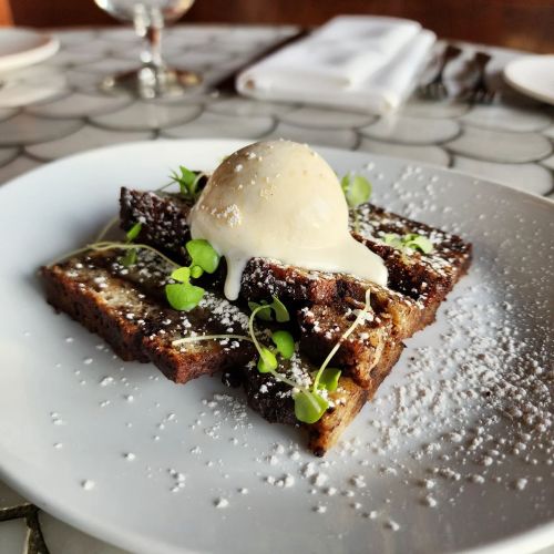 A plate of chocolate cake slices topped with vanilla ice cream, microgreens, and a dusting of powdered sugar.