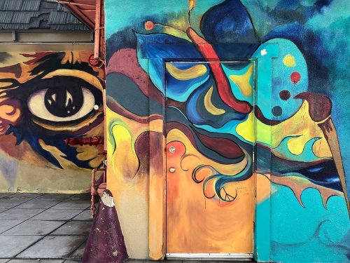 Colorful mural featuring abstract shapes and an eye, with a vibrant door blending into the artwork on a textured wall.