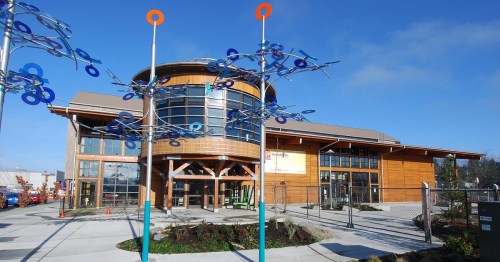 Modern wooden building with large windows, surrounded by colorful sculptures and a clear blue sky.