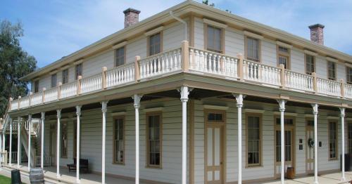A two-story historic building with a wraparound porch, featuring white siding and decorative columns.