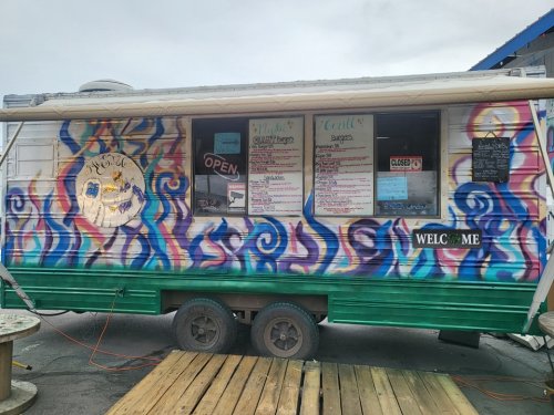 A colorful food truck with a painted design, featuring a menu board and a welcoming sign.