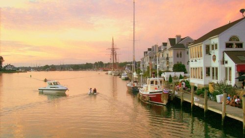 A serene waterfront scene at sunset, featuring boats and charming buildings along the shore.