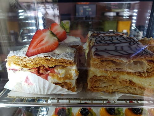 Two layers of pastry with cream and fruit, one topped with a strawberry and powdered sugar, the other with chocolate drizzle.