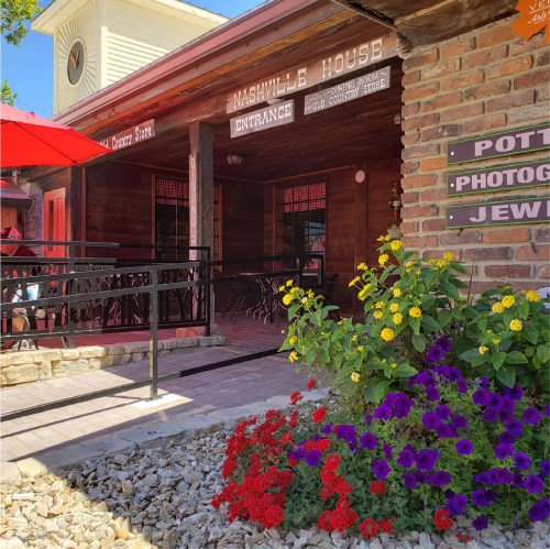 A rustic building with a sign reading "Nashville House," featuring colorful flowers and outdoor seating.