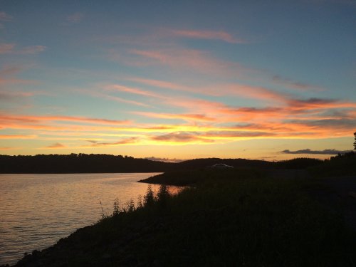 A serene sunset over a calm lake, with vibrant orange and pink clouds reflecting on the water's surface.