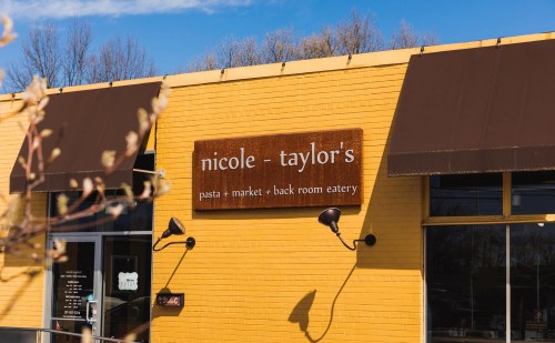 Sign for "nicole - taylor's" pasta market and back room eatery on a bright yellow building with a blue sky.