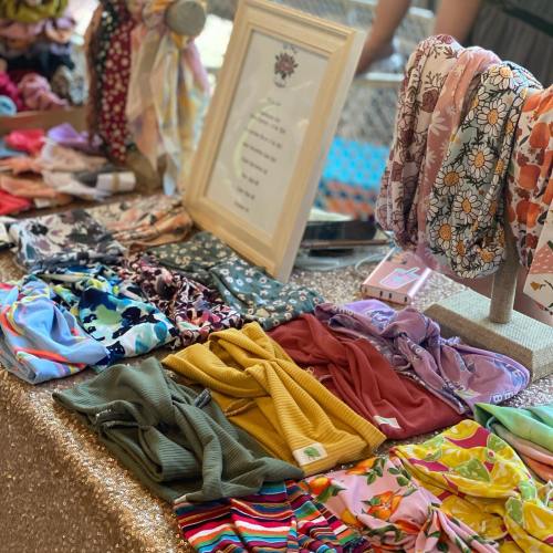 A display of colorful headbands and scarves on a table, with a framed sign in the background.