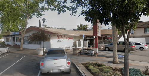 A liquor store with a sign reading "Café & Bottle Liquor" next to a parking area and trees.