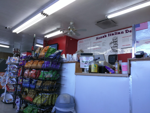 Interior of a deli featuring a menu board, snack displays, and a cash register area. Bright lighting and a casual atmosphere.