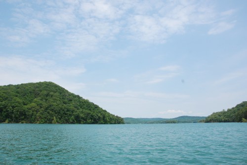A serene lake surrounded by lush green hills under a partly cloudy sky.