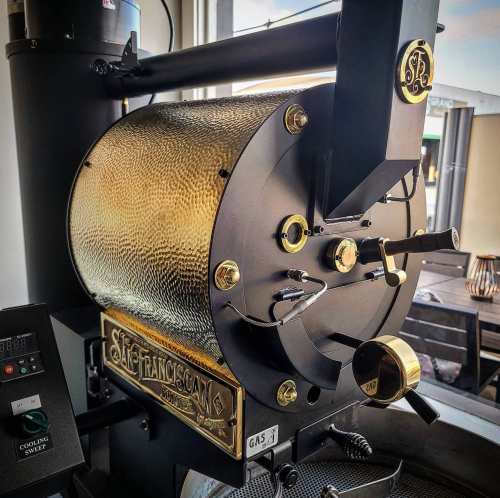 Close-up of a vintage-style coffee roaster with a shiny gold and black design, featuring dials and controls.