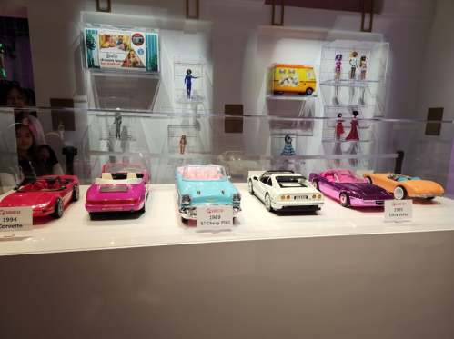 Display of vintage toy cars, including a pink Corvette, a 1957 Chevy, and various colorful models in a showcase.