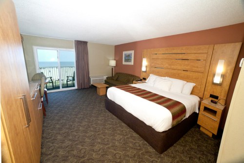 A cozy hotel room featuring a king-sized bed, seating area, and a balcony with ocean views.