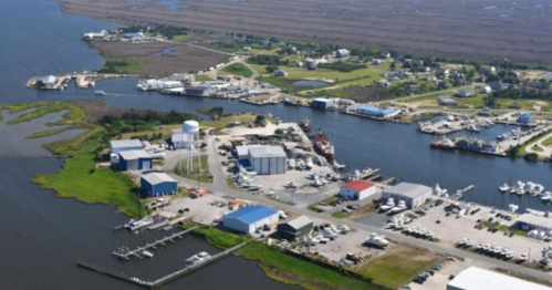 Aerial view of a coastal industrial area with buildings, a water tower, and boats along the waterway.