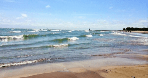 A serene beach scene with gentle waves, sandy shore, and a clear blue sky in the background.