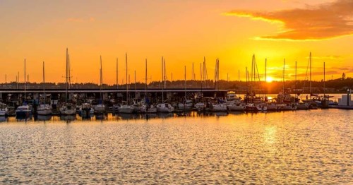 Sunset over a marina, with boats docked and reflections shimmering on the water.