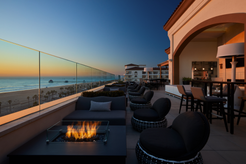 Rooftop lounge with modern seating, a fire pit, and ocean views at sunset.