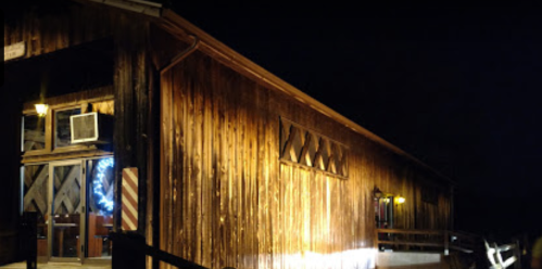 A wooden barn illuminated at night, featuring a blue wreath and warm lights on the exterior.