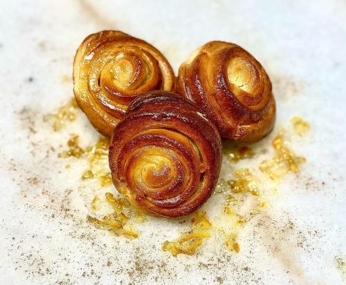 Three golden-brown spiral pastries on a marble surface, sprinkled with bits of caramelized sugar.