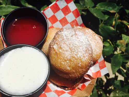A plate of golden-brown fried treats dusted with powdered sugar, served with two dipping sauces: one red and one white.