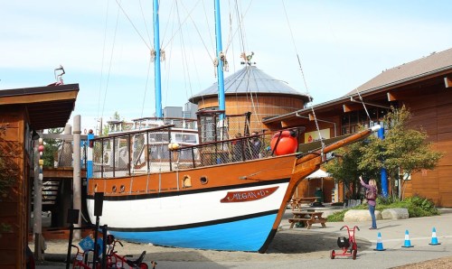 A wooden ship named "Megan D" docked in a harbor, surrounded by buildings and trees under a clear blue sky.