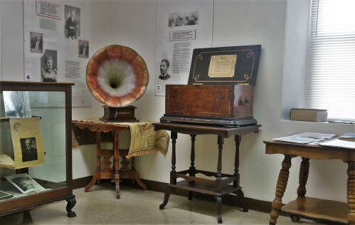 A vintage room displaying a gramophone, wooden cabinets, and historical photographs on the walls.