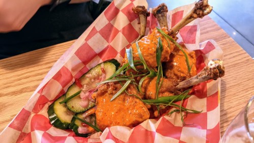 A basket of chicken wings topped with orange sauce, served with cucumber and onion salad on a checkered paper liner.