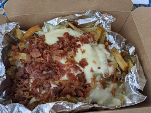 A box of loaded fries topped with melted cheese and crispy bacon bits.