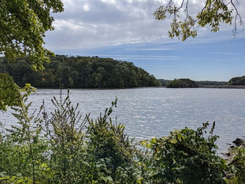 A serene lake surrounded by lush greenery and trees under a partly cloudy sky.