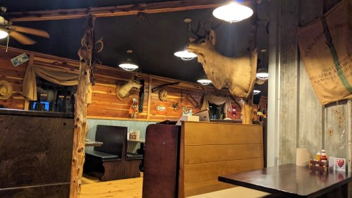 Interior of a rustic restaurant featuring wooden decor, a mounted deer head, and cozy seating areas.