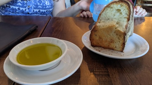 A plate with a slice of bread next to a small bowl of olive oil on a wooden table.