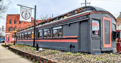A vintage train car restaurant with a sign reading "Open," surrounded by gravel and greenery.