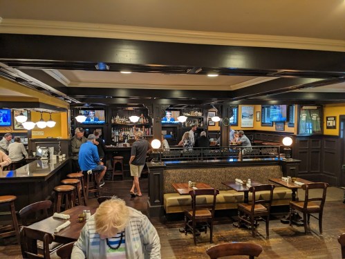A cozy restaurant interior with a bar, patrons seated at tables, and TVs showing sports in a warm, inviting atmosphere.