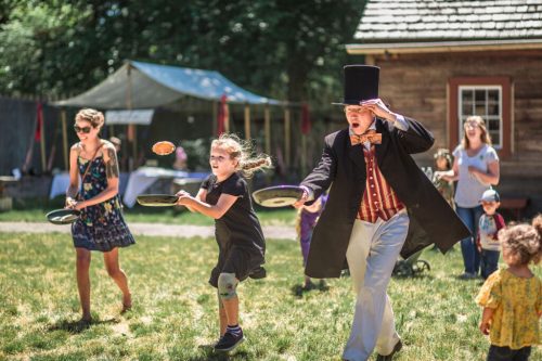 A lively outdoor scene with children and adults running, holding plates, and enjoying a festive atmosphere.