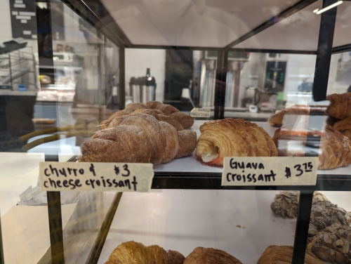 Display case with two croissants: a churro cheese croissant and a guava croissant, both priced at $3.00 and $3.25.