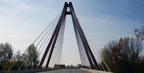 A modern cable-stayed bridge with a red framework and trees in the background under a clear blue sky.
