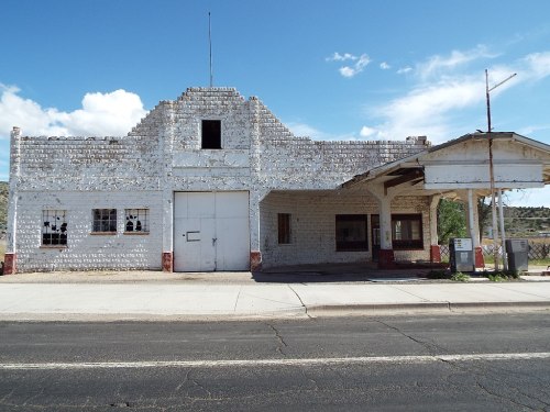 Abandoned white building with broken windows and a covered porch, set against a blue sky.